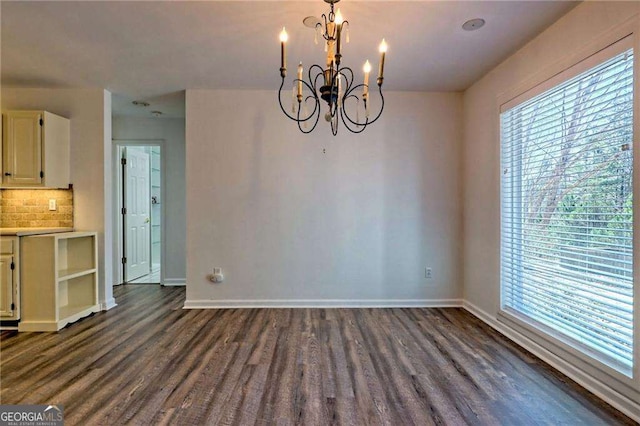 unfurnished dining area with dark wood-style floors, plenty of natural light, baseboards, and an inviting chandelier