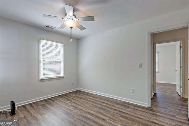 empty room with dark wood-style floors, visible vents, baseboards, and ceiling fan