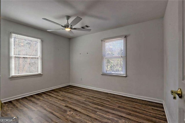 empty room with dark wood-type flooring, a ceiling fan, visible vents, and baseboards