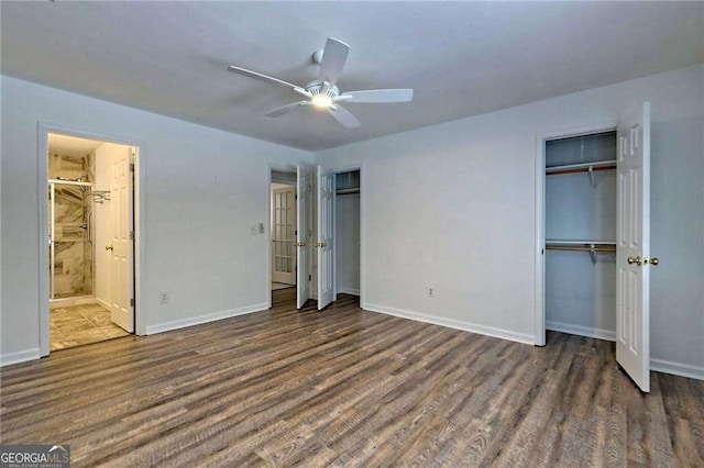 unfurnished bedroom featuring connected bathroom, baseboards, dark wood-type flooring, and two closets