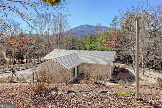 view of property exterior featuring central AC, a mountain view, a tiled roof, and fence