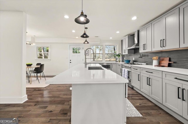 kitchen with stainless steel range, tasteful backsplash, light countertops, a sink, and wall chimney exhaust hood