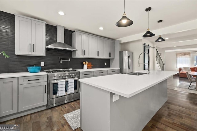 kitchen with a barn door, stainless steel appliances, dark wood-style flooring, a sink, and wall chimney exhaust hood