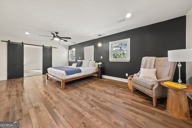 bedroom featuring a barn door, visible vents, baseboards, and light wood-style flooring