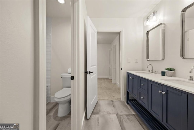 bathroom with double vanity, baseboards, toilet, and a sink