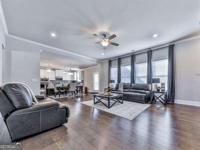 living area with a ceiling fan, baseboards, ornamental molding, and dark wood-style flooring