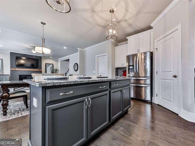 kitchen with white cabinetry, open floor plan, stainless steel refrigerator with ice dispenser, a center island with sink, and pendant lighting