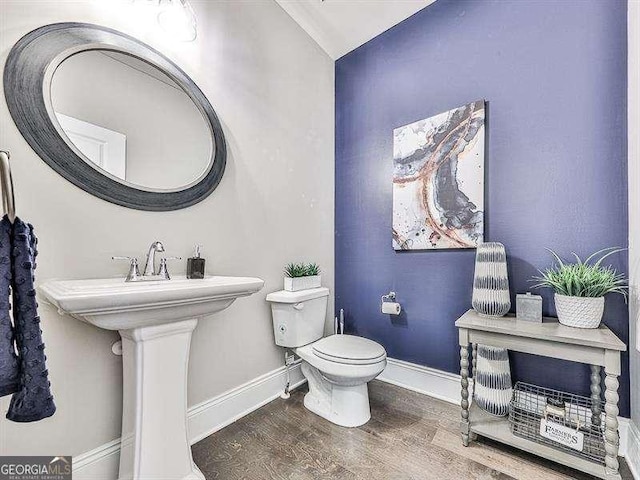 half bath with baseboards, toilet, and wood finished floors