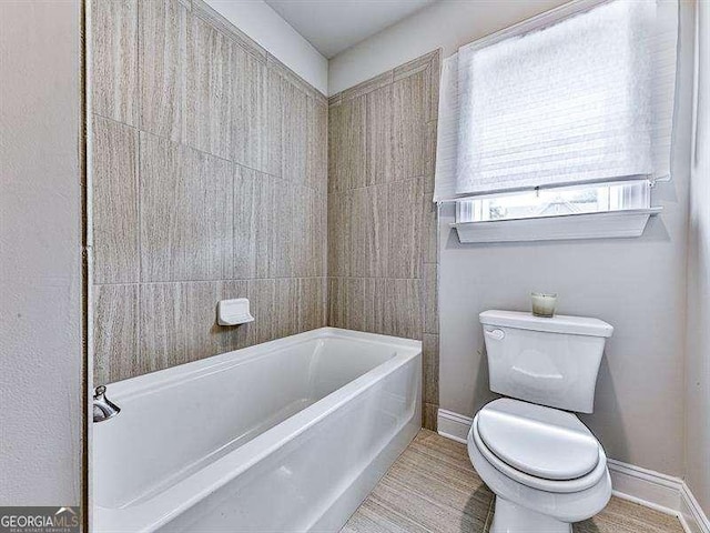 bathroom with toilet, baseboards, and a bath