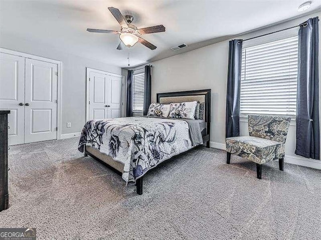 carpeted bedroom featuring baseboards, visible vents, ceiling fan, and two closets