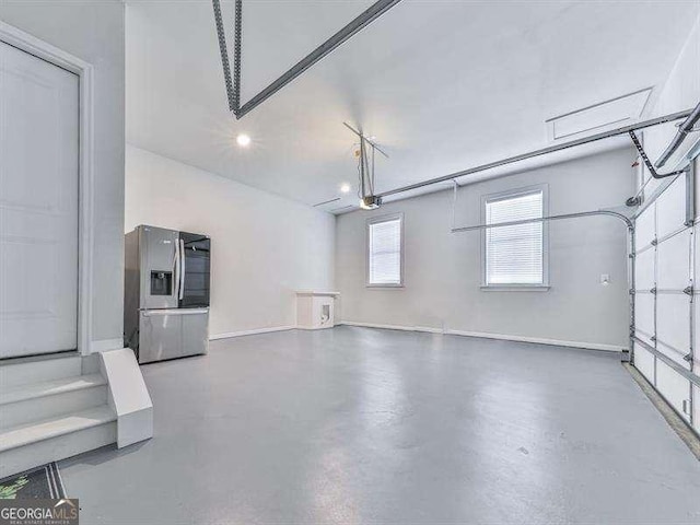 garage featuring baseboards, stainless steel refrigerator with ice dispenser, and a garage door opener