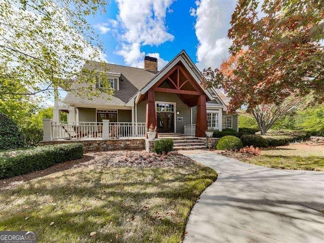 craftsman house with covered porch, a chimney, and a front yard