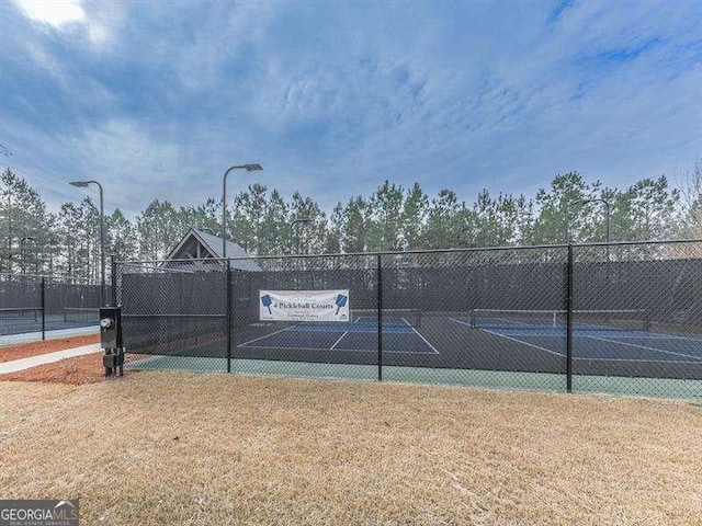 view of tennis court with a yard and fence