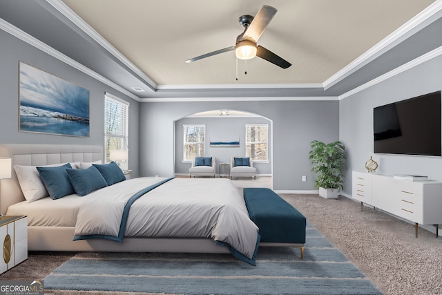 carpeted bedroom with arched walkways, a raised ceiling, ornamental molding, a ceiling fan, and baseboards