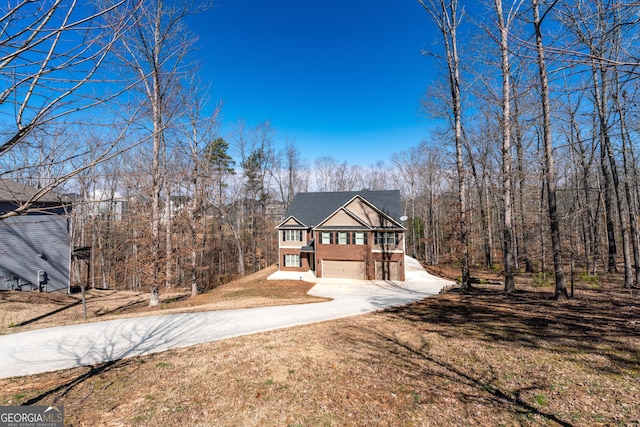 view of front of property featuring a forest view, brick siding, driveway, and a front lawn