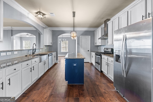 kitchen featuring arched walkways, a kitchen island, a sink, appliances with stainless steel finishes, and wall chimney exhaust hood