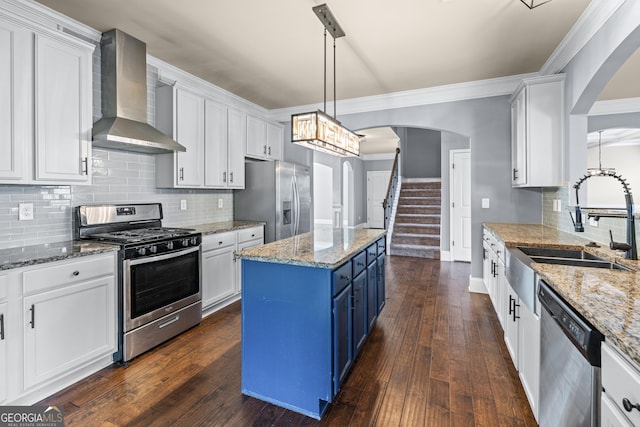 kitchen featuring blue cabinetry, stainless steel appliances, a sink, wall chimney range hood, and a kitchen island