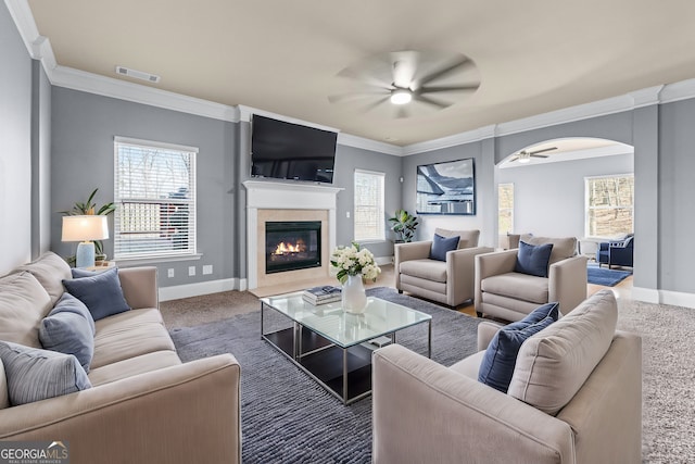 living area featuring arched walkways, visible vents, a fireplace with flush hearth, a ceiling fan, and baseboards