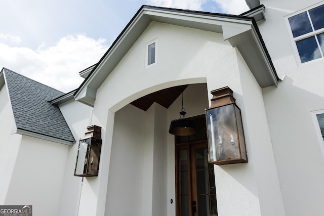 entrance to property with a shingled roof and stucco siding