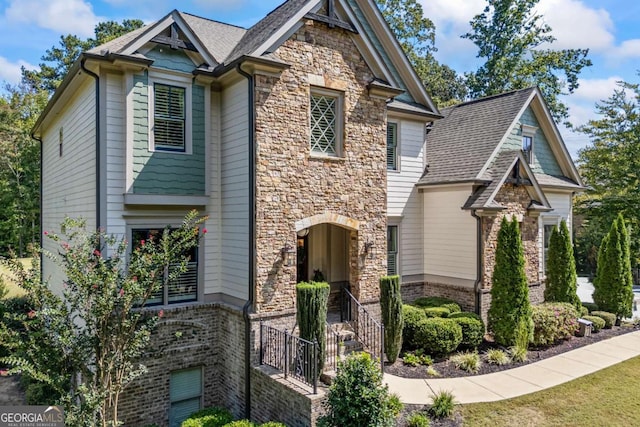 craftsman inspired home featuring stone siding, a shingled roof, and brick siding