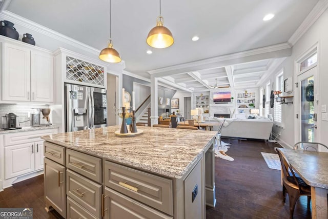 kitchen with white cabinets, open floor plan, a lit fireplace, stainless steel fridge, and a kitchen bar