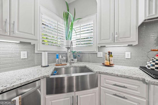 kitchen featuring tasteful backsplash, white cabinets, light stone countertops, stainless steel dishwasher, and a sink