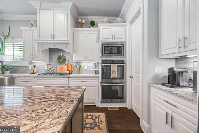 kitchen featuring appliances with stainless steel finishes, white cabinets, ornamental molding, and light stone countertops