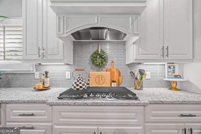 kitchen featuring tasteful backsplash, white cabinets, stainless steel gas stovetop, and light stone countertops