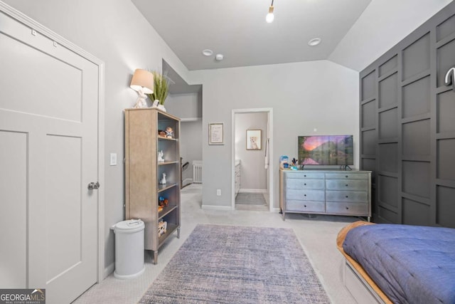 bedroom featuring lofted ceiling, baseboards, ensuite bathroom, and light colored carpet