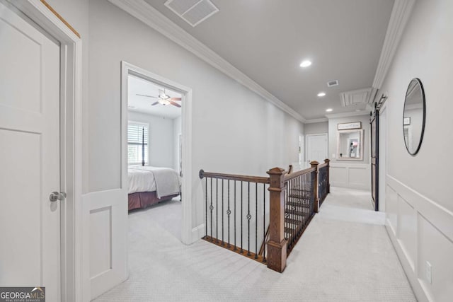 hall featuring a decorative wall, light colored carpet, visible vents, an upstairs landing, and ornamental molding