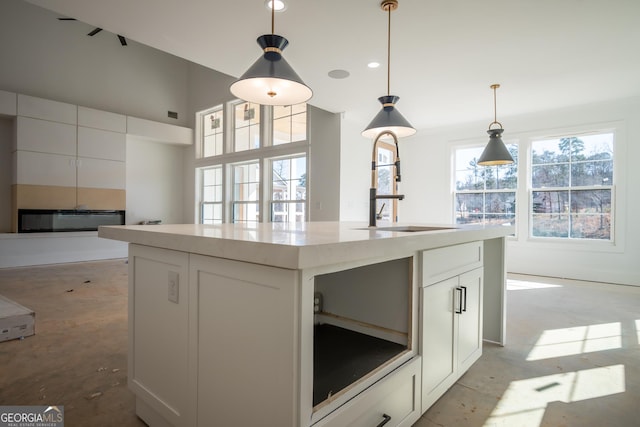 kitchen featuring a sink, white cabinets, light countertops, an island with sink, and decorative light fixtures