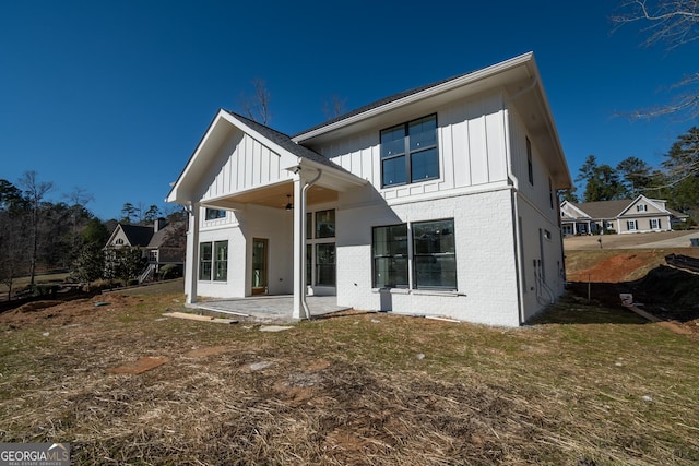 back of property with a patio, brick siding, board and batten siding, and a lawn