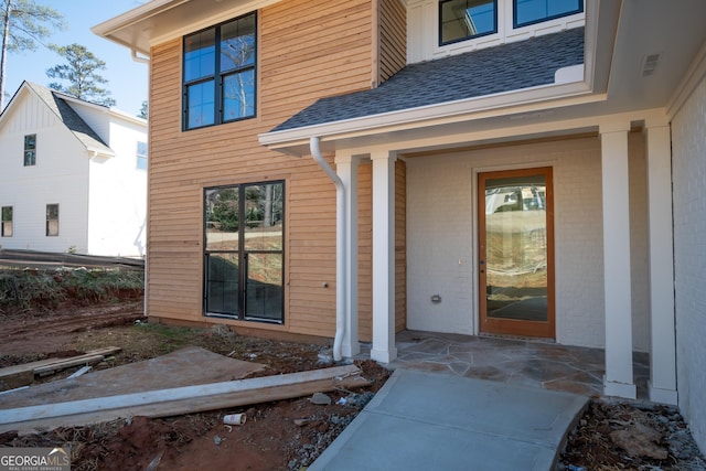 doorway to property with a shingled roof and brick siding