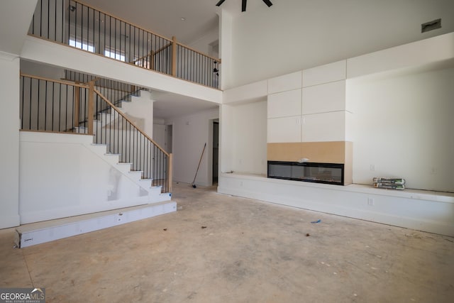 unfurnished living room featuring concrete flooring, visible vents, a towering ceiling, stairs, and a glass covered fireplace