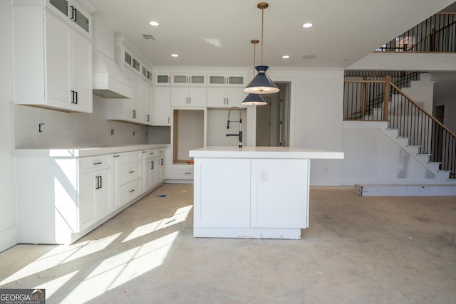 kitchen with pendant lighting, light countertops, glass insert cabinets, a kitchen island with sink, and white cabinets