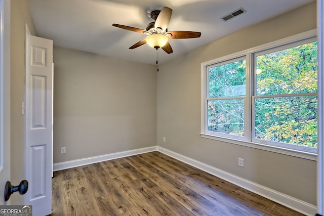 empty room featuring a ceiling fan, visible vents, baseboards, and wood finished floors