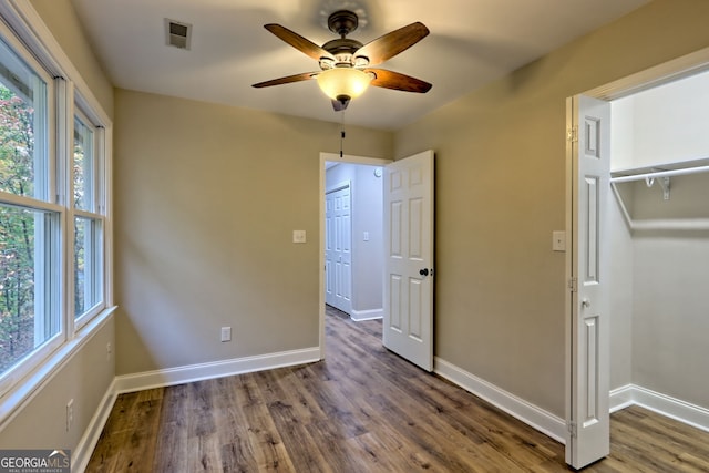 unfurnished bedroom featuring multiple windows, dark wood finished floors, visible vents, and baseboards