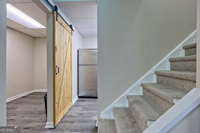 stairway with wood finished floors, a drop ceiling, baseboards, and a barn door