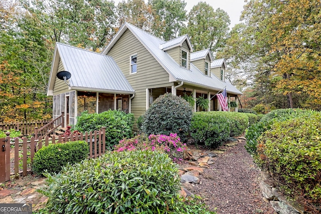 new england style home with metal roof, fence, and a sunroom