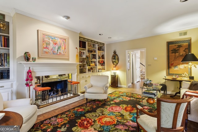 sitting room with a fireplace with raised hearth, built in shelves, visible vents, baseboards, and ornamental molding