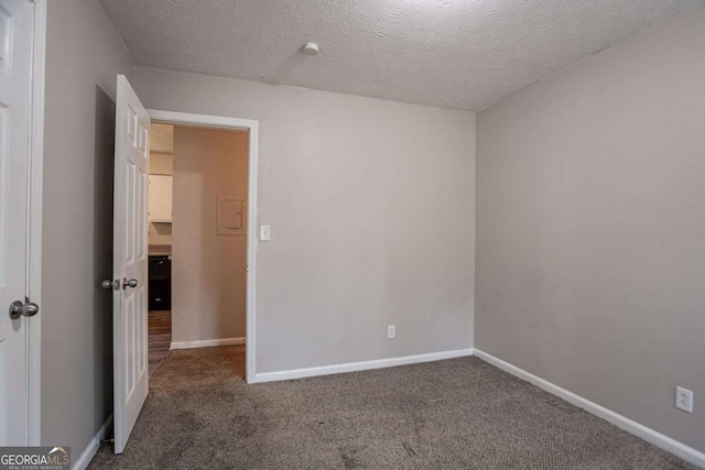 unfurnished room with a textured ceiling, dark colored carpet, and baseboards