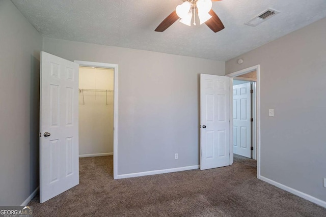 unfurnished bedroom with a textured ceiling, a spacious closet, carpet floors, and visible vents