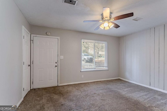 empty room featuring a textured ceiling, carpet floors, visible vents, baseboards, and a ceiling fan