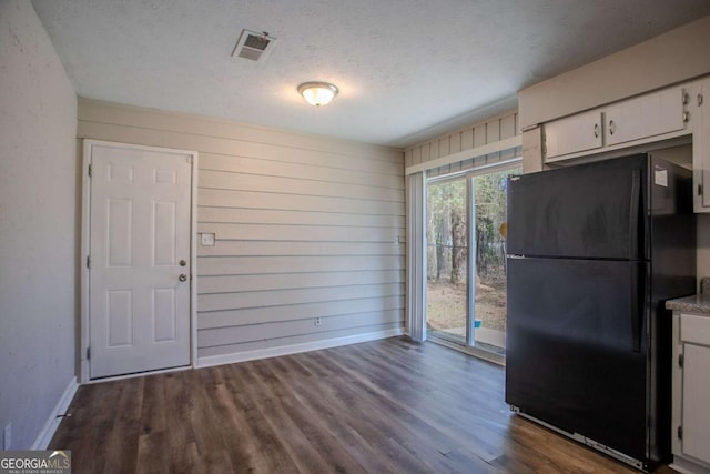 unfurnished dining area featuring a textured ceiling, wooden walls, wood finished floors, visible vents, and baseboards