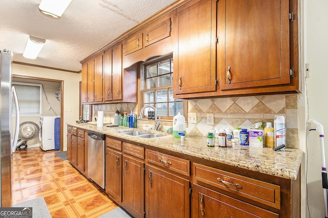 kitchen featuring light stone counters, brown cabinets, washer and clothes dryer, stainless steel appliances, and a sink