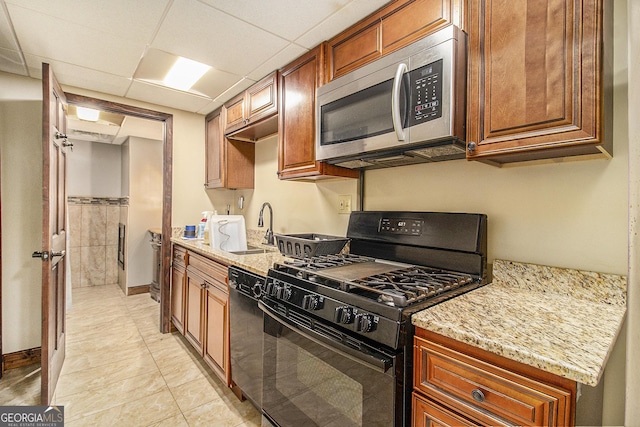 kitchen with a paneled ceiling, light stone countertops, a sink, brown cabinets, and black appliances