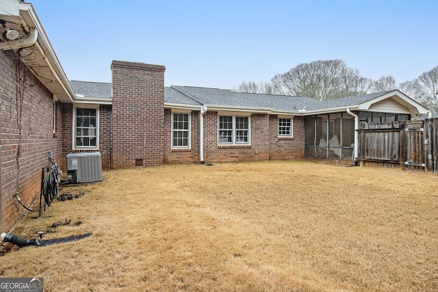 back of property with brick siding, a chimney, a lawn, a sunroom, and central AC