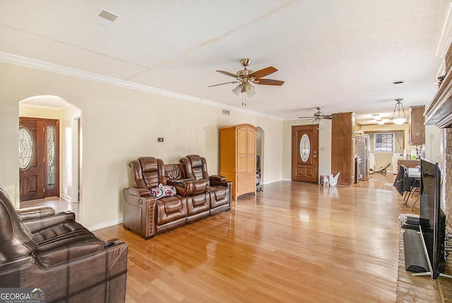 living area with arched walkways, light wood-style flooring, ornamental molding, a ceiling fan, and baseboards