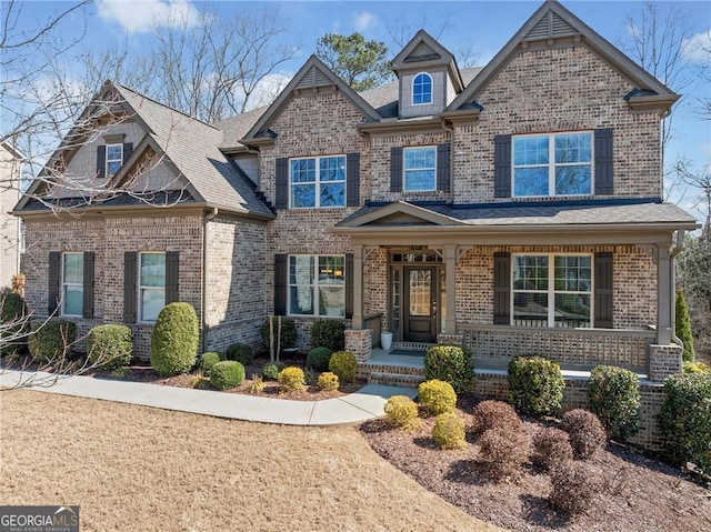 craftsman-style house with a shingled roof, covered porch, and brick siding