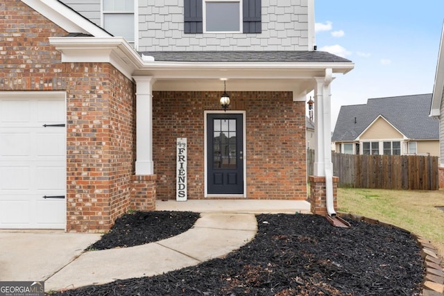 view of exterior entry with brick siding, a porch, a shingled roof, fence, and a garage